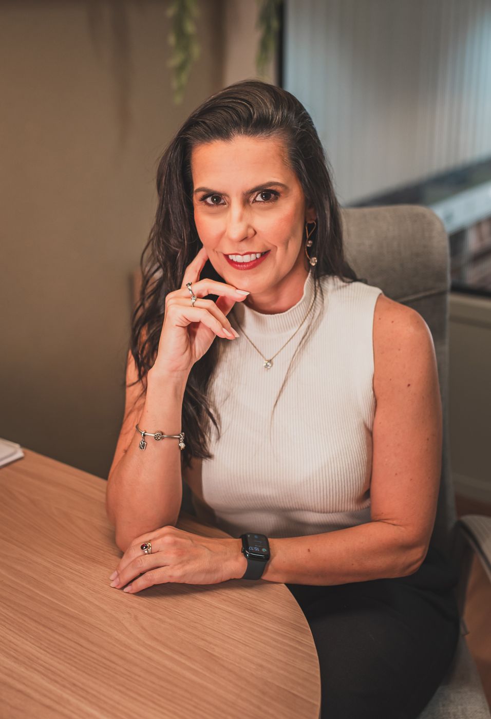 Simone Afonso sorrindo, com a mão perto do queixo, sentada à mesa