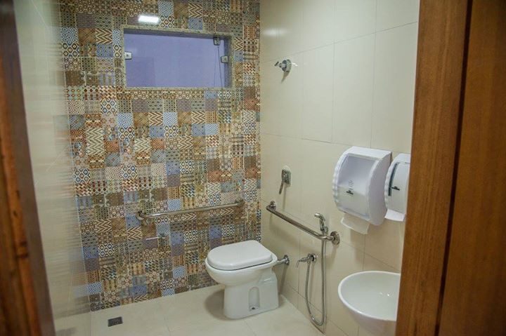 Banheiro acessível com parede de azulejos estampados coloridos, barras de apoio e bancada de madeira