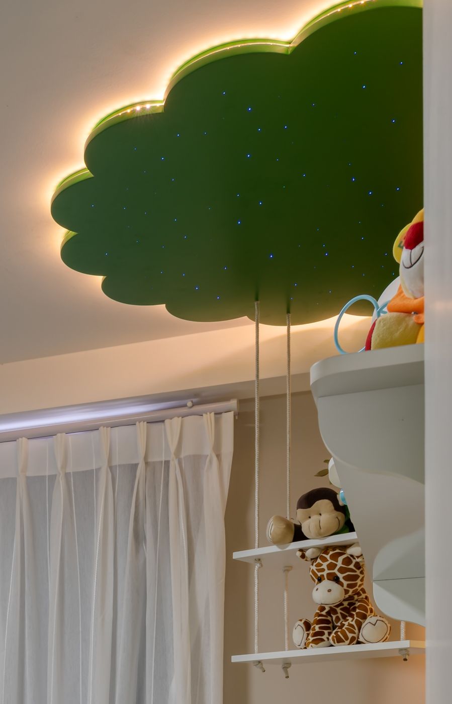 Quarto de bebê com nuvem verde iluminada, cortina branca e prateleira com bichos de pelúcia