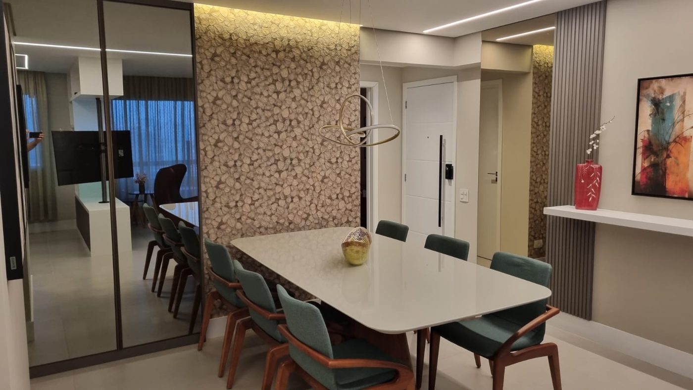 Mesa de jantar clara com cadeiras verdes, parede de pastilhas e porta espelhada